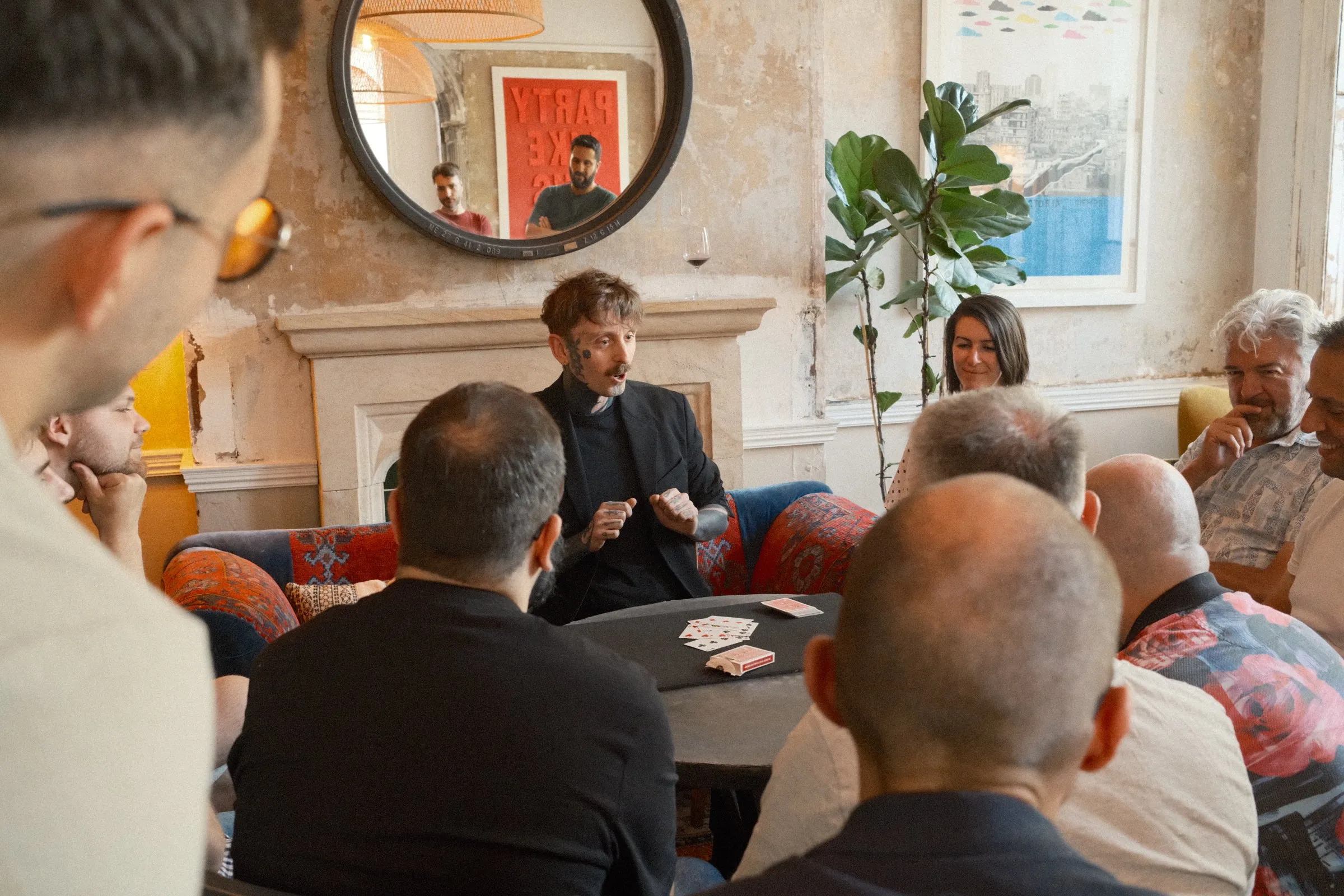 Si performing close-up magic to a seated group at a private corporate event, with cards fanned on the table