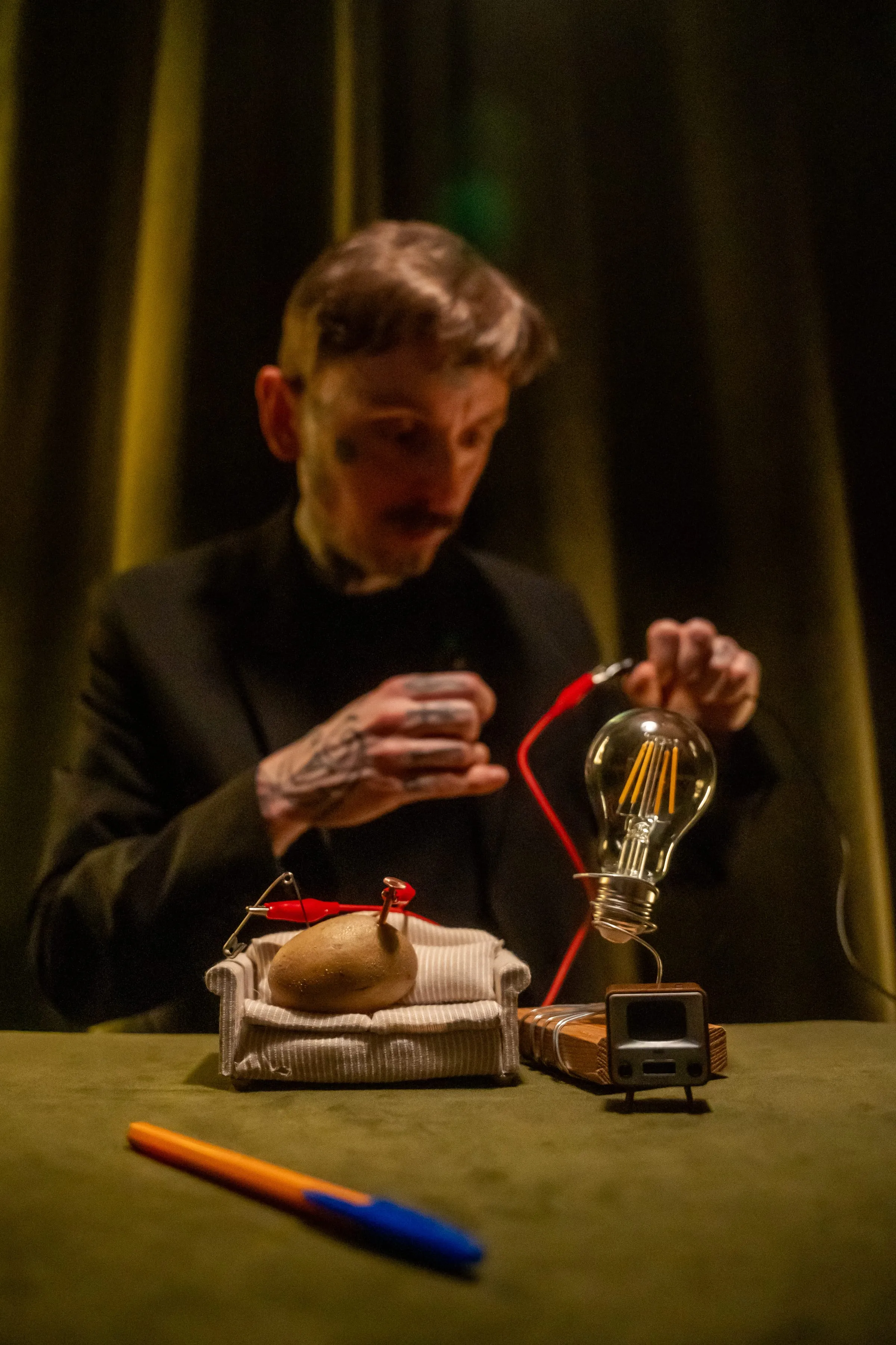 Surreal close-up magic with a light-bulb prop against green velvet curtains