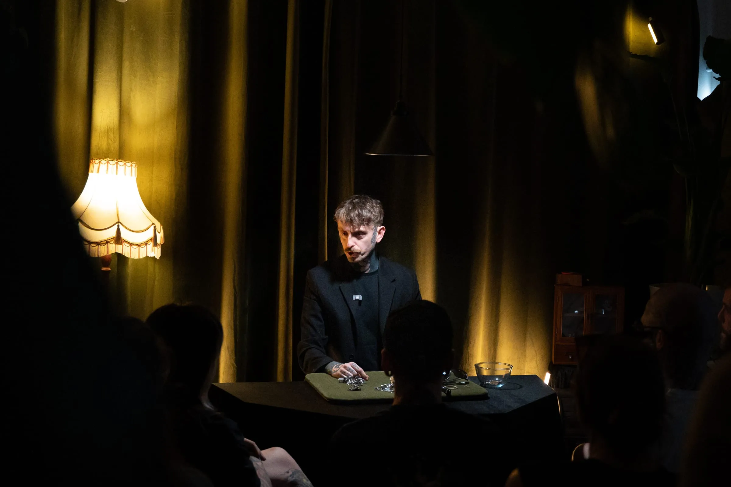 Si at the lamplit table mid-routine, watched by the front row